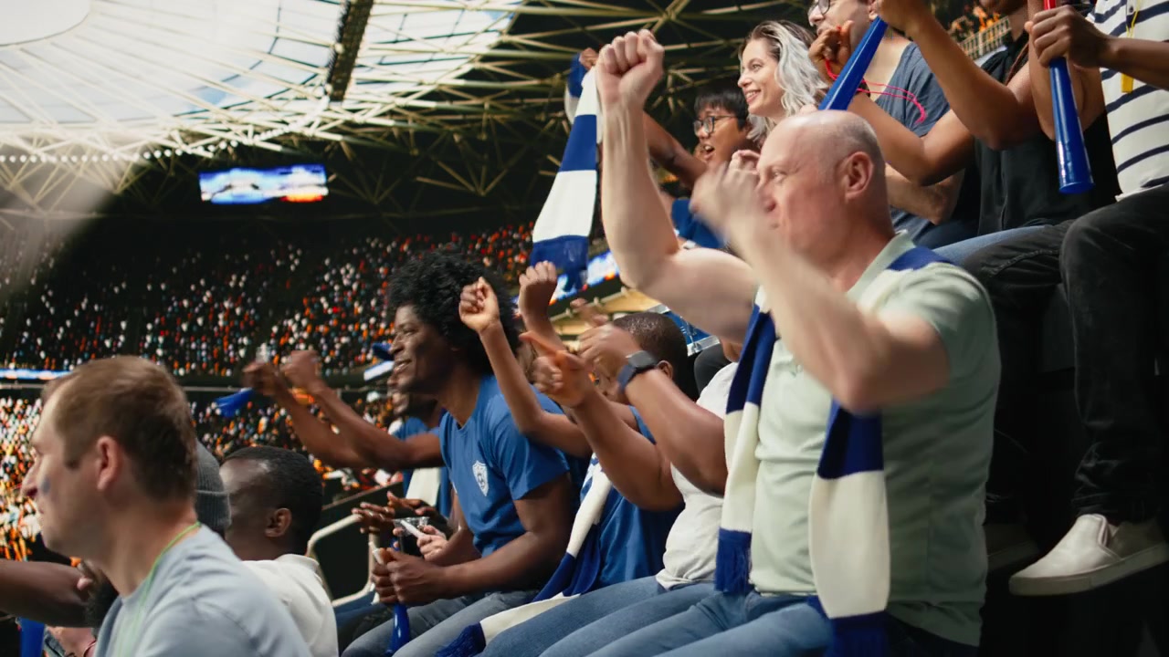 Aficionados tensos del equipo azul reaccionando a una jugada apretada durante un partido de fútbol en vivo