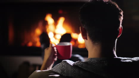 young successful man resting with a cup of tea by the fireplace