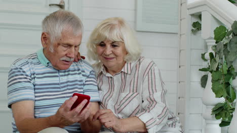 senior elderly caucasian couple using mobile phone in porch at home. enjoy online shopping, news