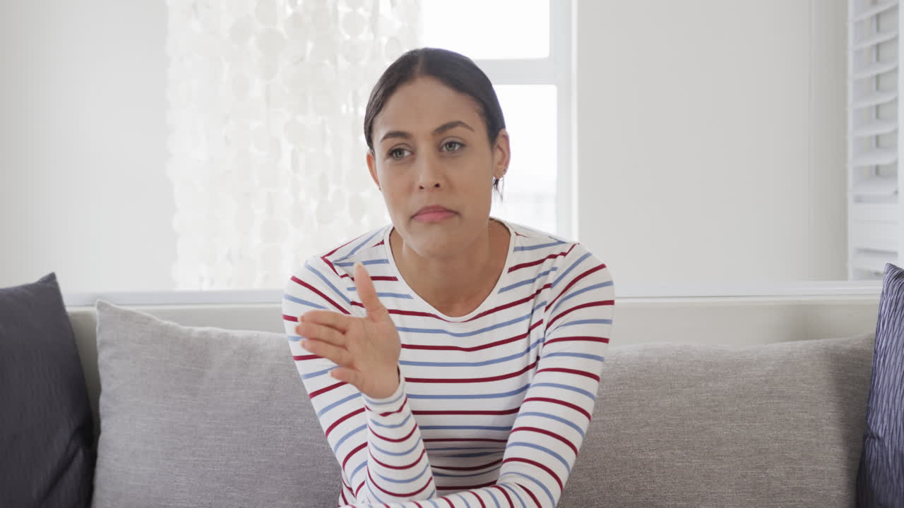 mujer biracial sentada en el sofá haciendo una llamada de video, en cámara lenta