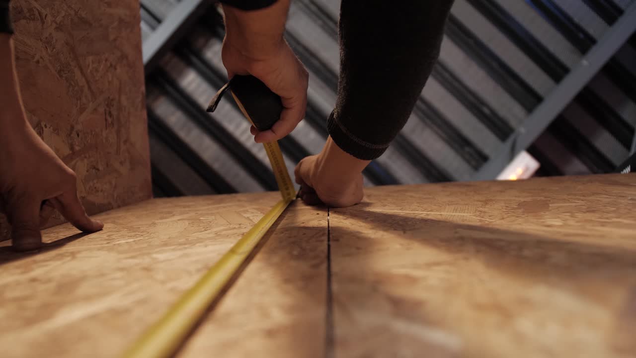 Hands measuring plywood surface with tape measure indoors - close-up