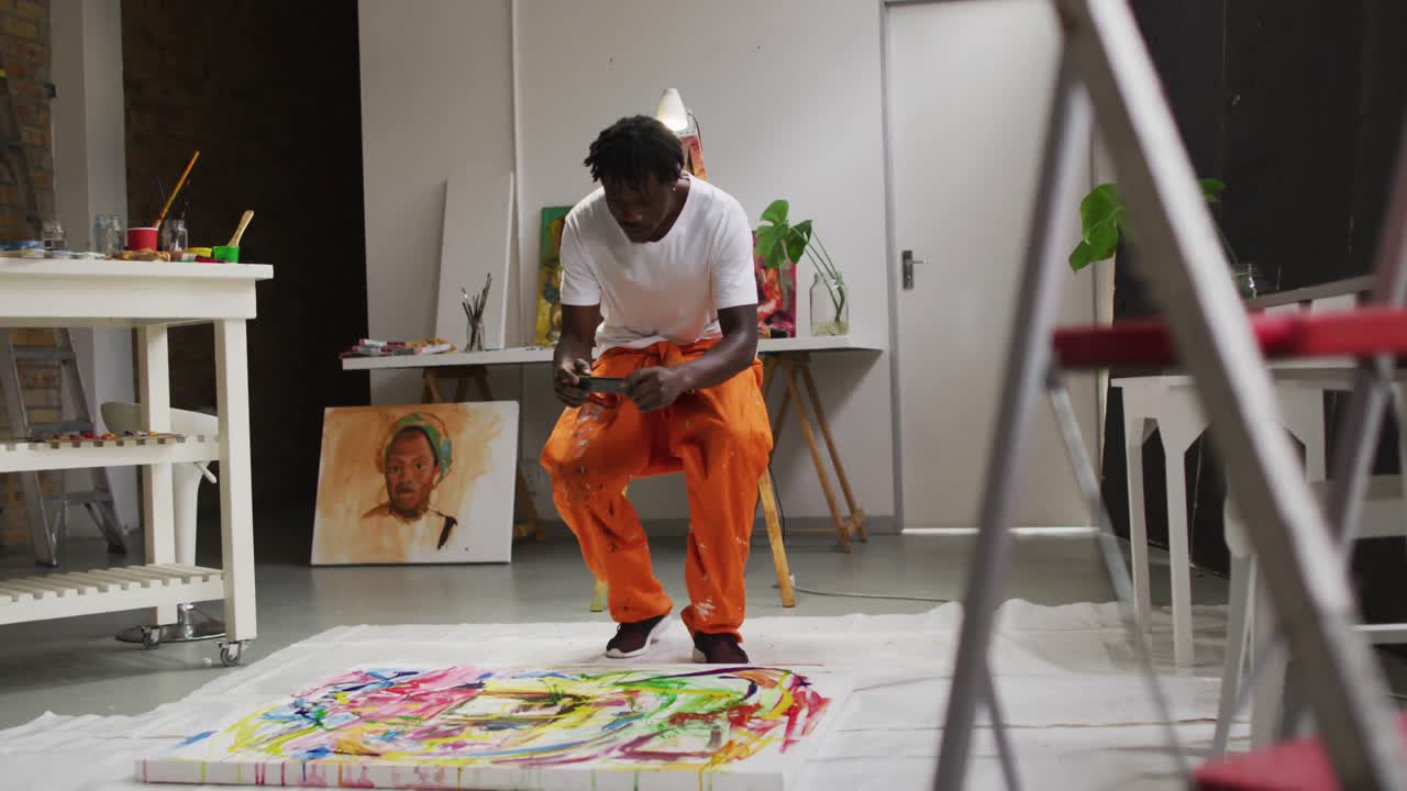 African american male artist taking a picture of his painting with a smartphone at art studio