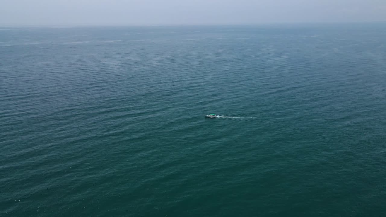 Aerial drone shot showcasing a small fisher boat drifting in the heart of the open ocean.