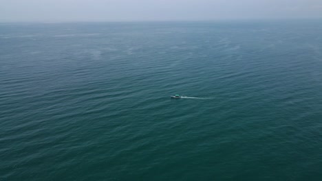 aerial drone shot showcasing a small fisher boat drifting in the heart of the open ocean.