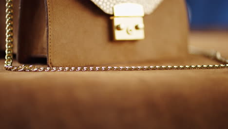 close-up of a stylish brown suede handbag with gold chain and metallic details