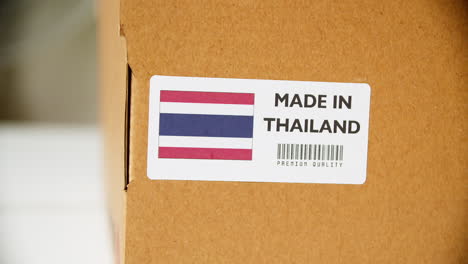 manos aplicando etiqueta de bandera hecha en tailandia en una caja de cartón de envío con productos