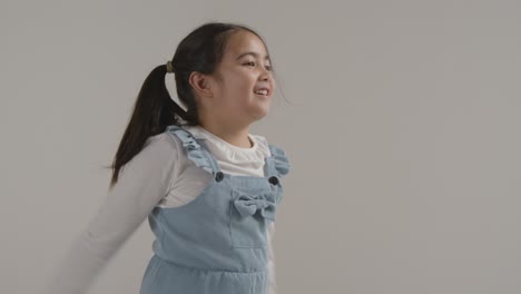 Studio-Portrait-Of-Hyperactive-Girl-Jumping-Against-White-Background