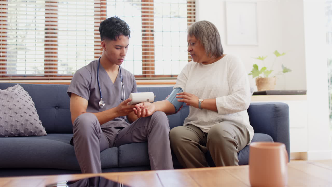 Measuring blood pressure, male nurse assisting senior woman on couch at home