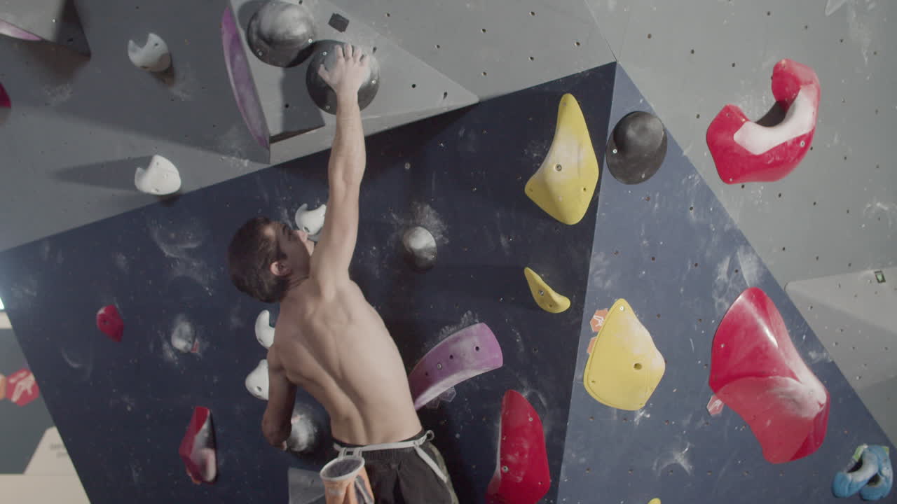 fuerte atleta masculino escalando una pared de roca artificial en el gimnasio de boulder
