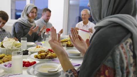 moderne multi-etnische moslimfamilie bidden voor het iftar diner samen tijdens een ramadan feest thuis