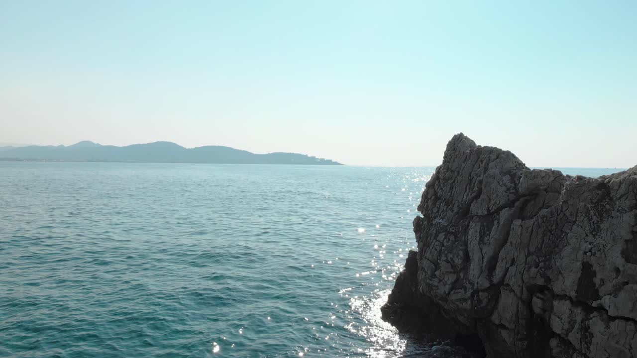 바다의 바위 옆에 있는 물 위의 낮은 드론 샷