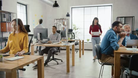 in the stylish modern office: diverse group of enthusiastic business marketing professionals use computers, have meetings, discussing project ideas, brainstorming startup company strategy