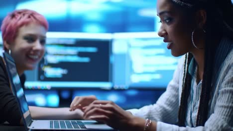 two women collaborate on a coding project in a high-tech environment, focused on problem-solving and digital solutions with screens displaying code behind them