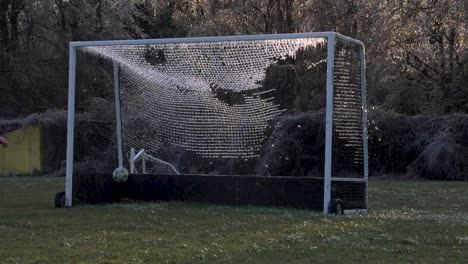 cámara lenta: una pelota de fútbol golpea una red helada de una portería de fútbol que explota hielo roto en el aire