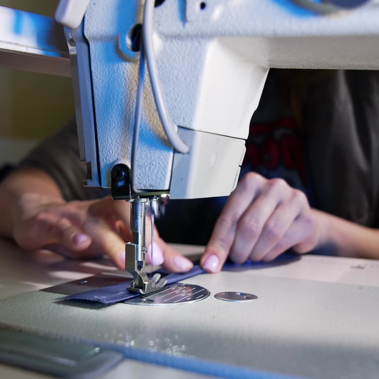 Process of sewing fabric on a sewing machine. Tailor working with sewing machine at workshop. Female's hand pushing material through sewing machine