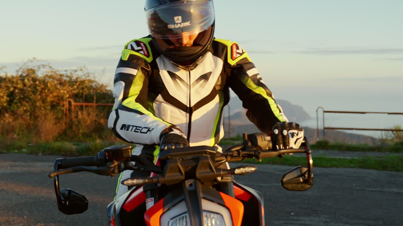 Motorcyclist adjusts his sport bike at sunset near a scenic coastal road, wearing full gear