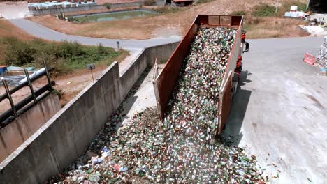 Truck-is-unloading-glass-on-concrete-surface-in-a-warehouse,-drone-view,-glass-recycling-in-a-processing-center-concept