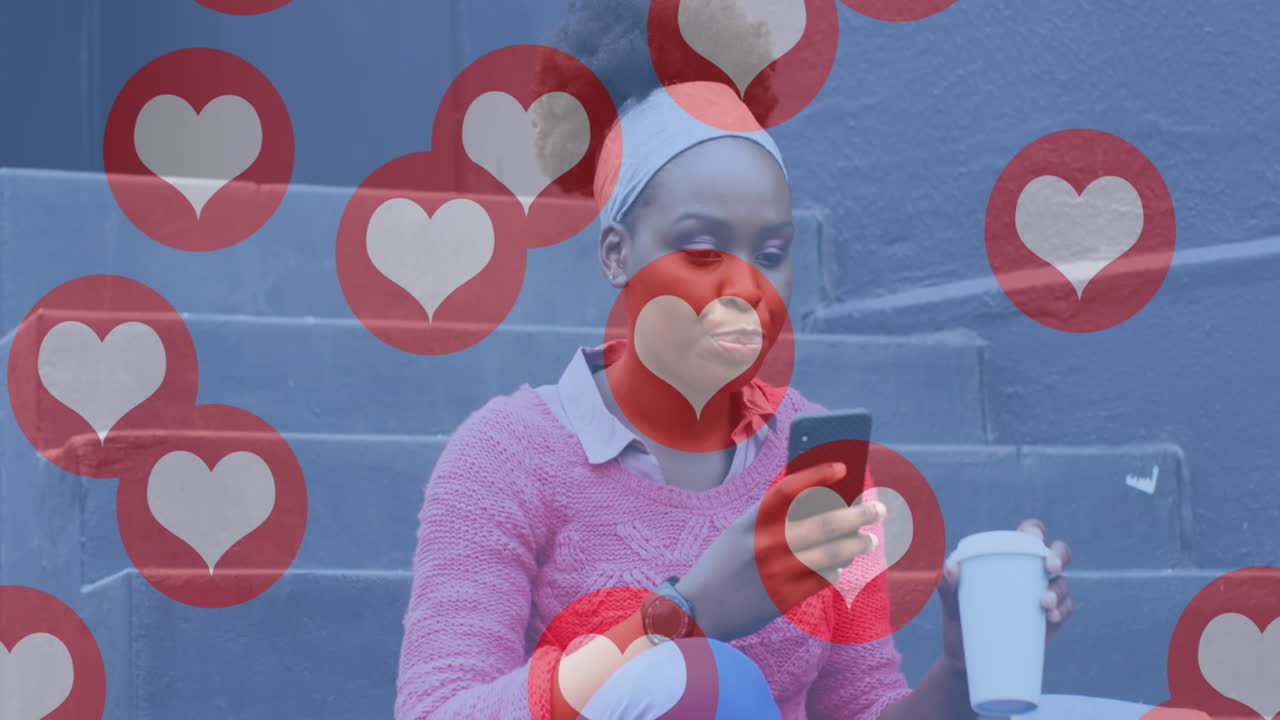 Animation of social media heart icons over happy african american woman in street using smartphone