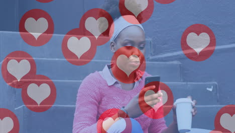 animation of social media heart icons over happy african american woman in street using smartphone