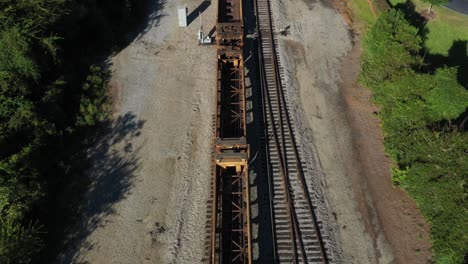 Aerial-view-of-rusty-train-cars-moving-along-a-straight-set-of-tracks-on-a-sunny-day-in-the-morning