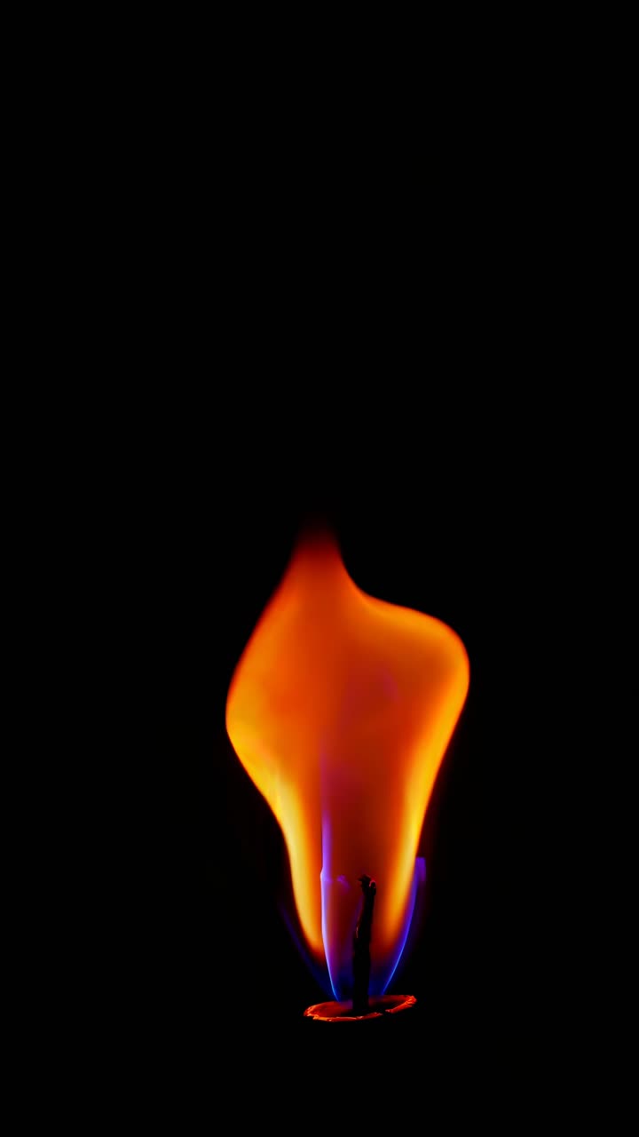 Close-up video still of a single flame against a black background, captured from a low angle