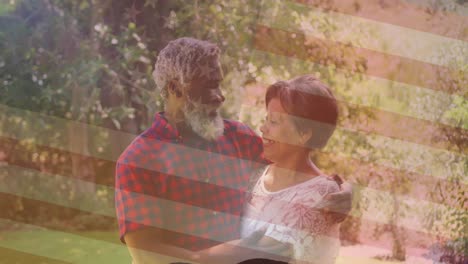 animación de la bandera nacional de américa sobre una feliz pareja de ancianos afroamericanos abrazándose en el parque
