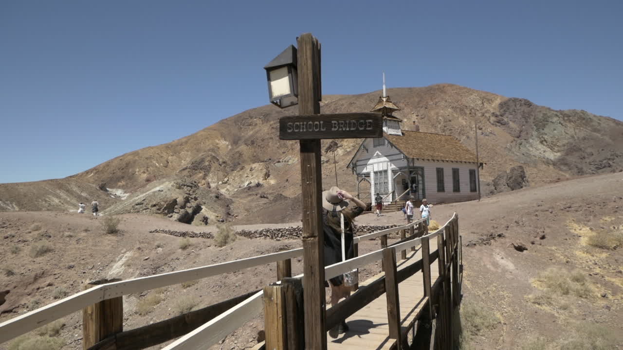 A young woman's hat almost blows off crossing a narrow wooden bridge, Calico Ghost Town, California
