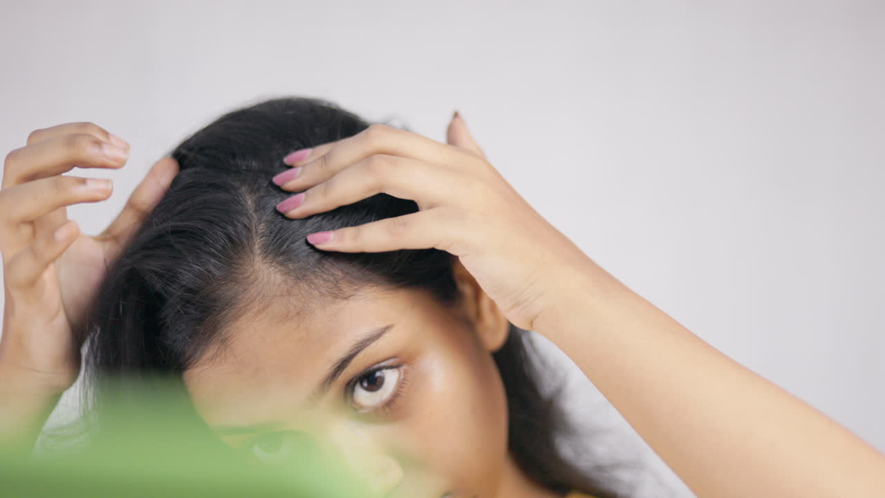 Androgenic alopecia, balding scalp, hairloss, a young woman examining her balding area in white background.