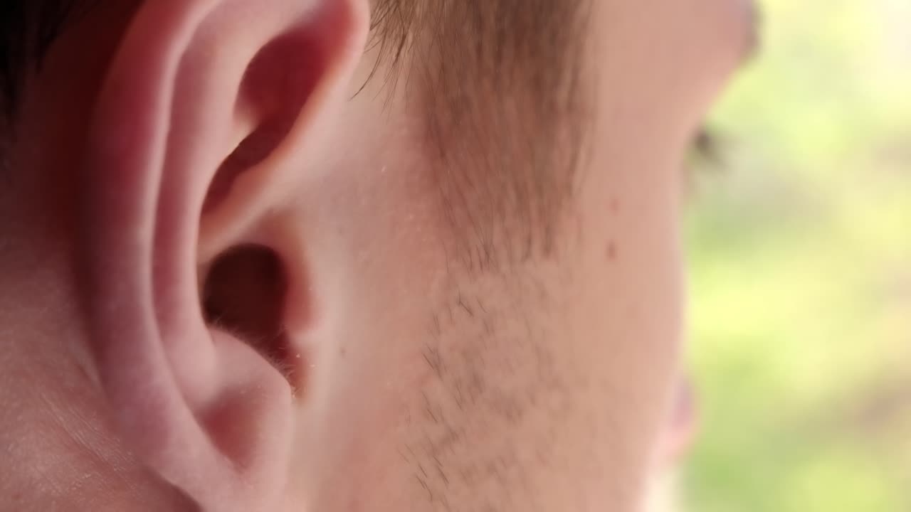 Caucasian man putting black wireless earbud in the ear. Rear view. Close up