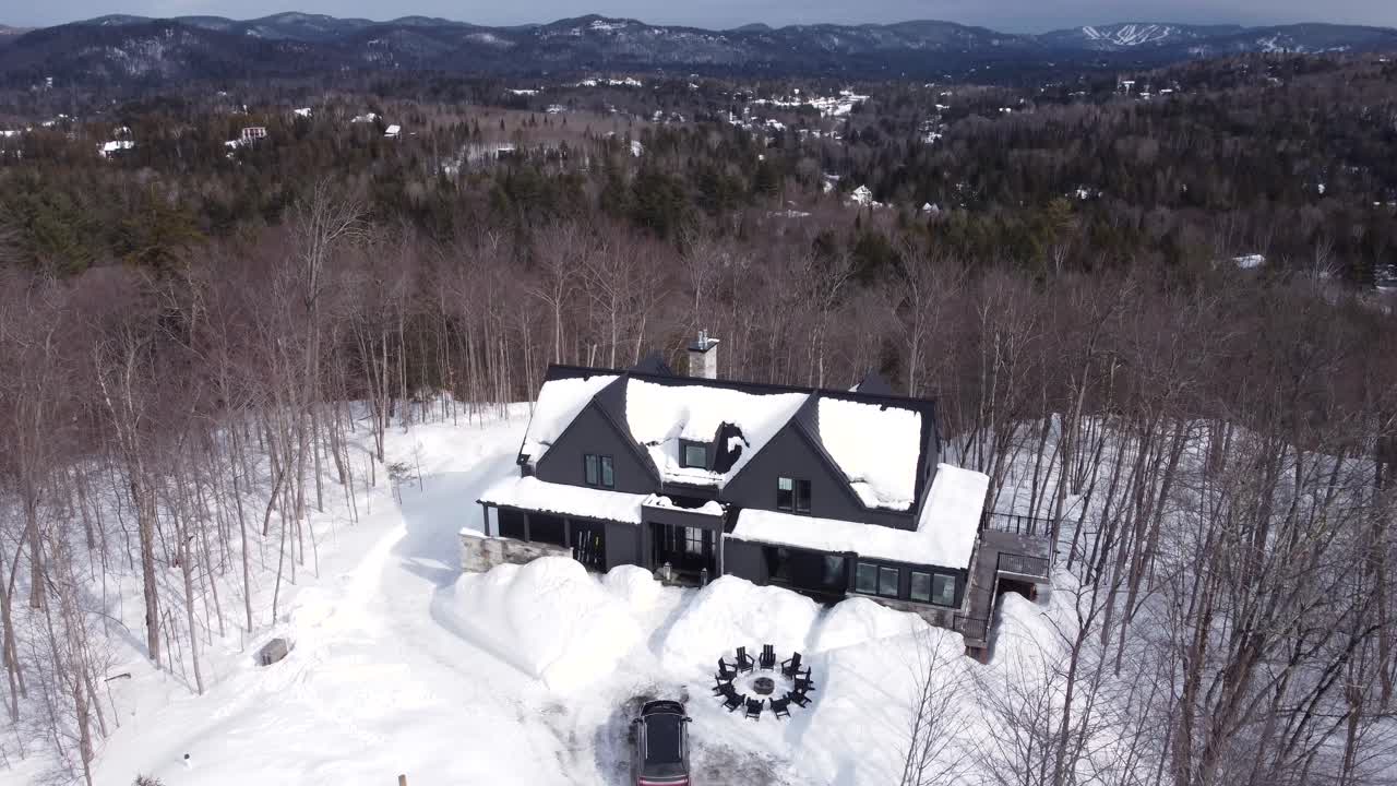 disparo aéreo panorámico hacia abajo a un chalet de lujo cubierto de nieve en invierno con un suv negro estacionado en la parte delantera