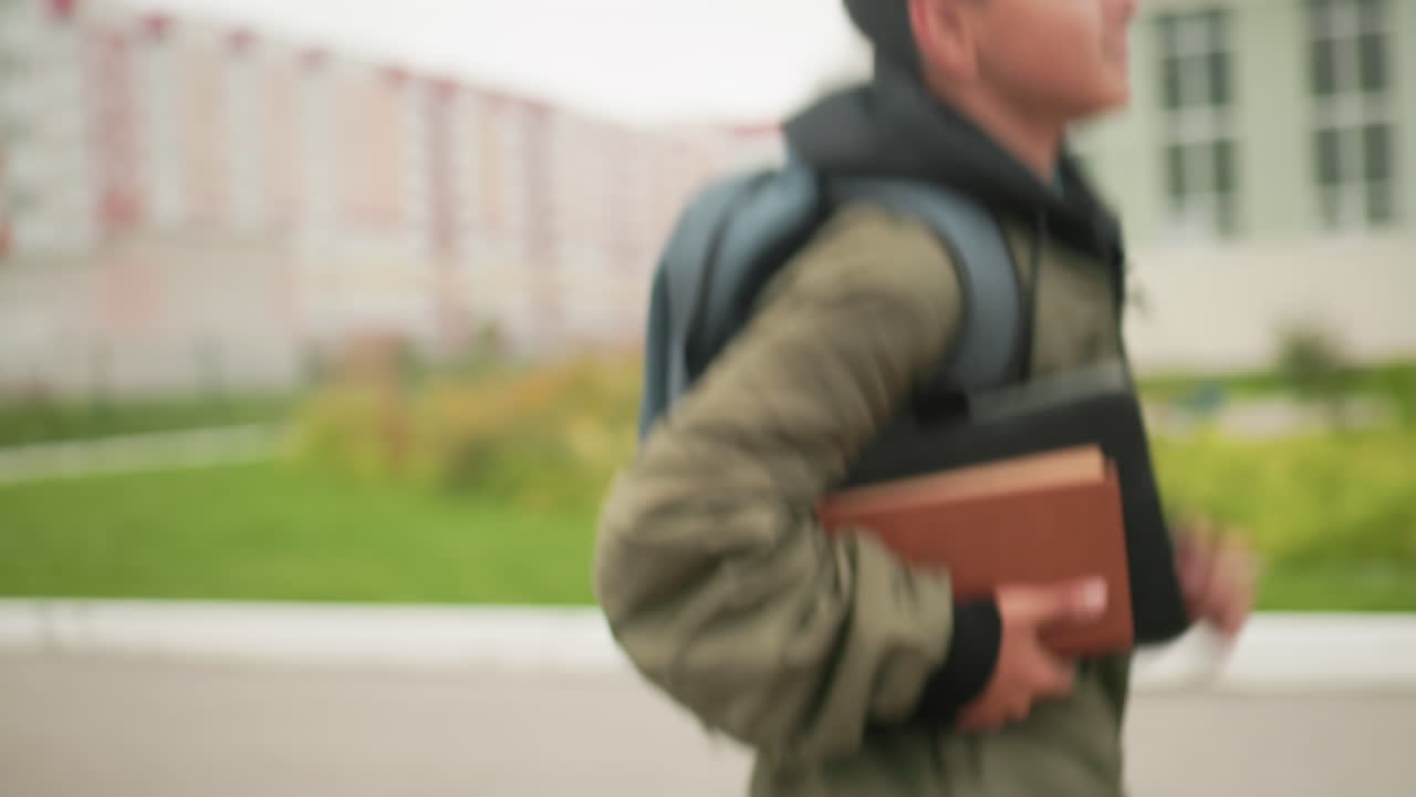 초록색 재킷을 입고 공책을 옆구리에 낀 어린 소년이 학교 계단에 다가갈수록 속도를 줄이며 책을 들고 결연하고 집중된 표정으로 달려가는 모습의 클로즈업 측면 뷰