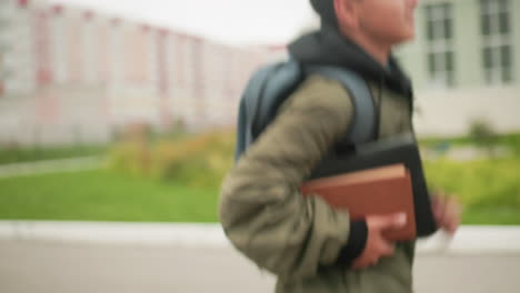 close up side view of young boy in green jacket running with notepad under arm slowing down as he approaches school steps carrying books with determination and focus