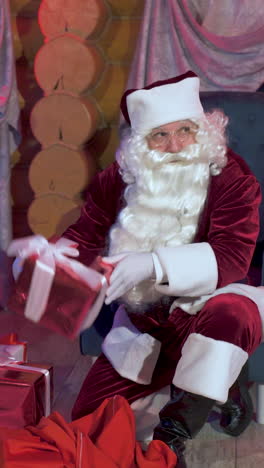 surprise under the christmas tree. santa with christmas presents in the house. old santa taking out gifts from his red bag. vertical video