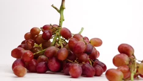 juicy red grape bunches on the vine falling into a pile on white table top in slow motion