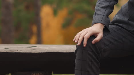 Guy-in-checkered-office-suit-taps-on-knee-sitting-on-bench