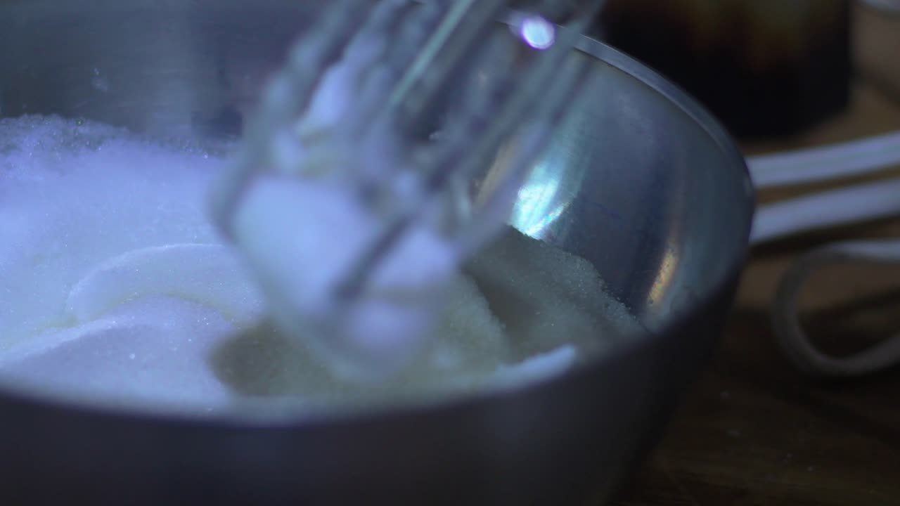 Close-up adding sugar to vigorously whipped, frothy white egg white in shiny metal bowl