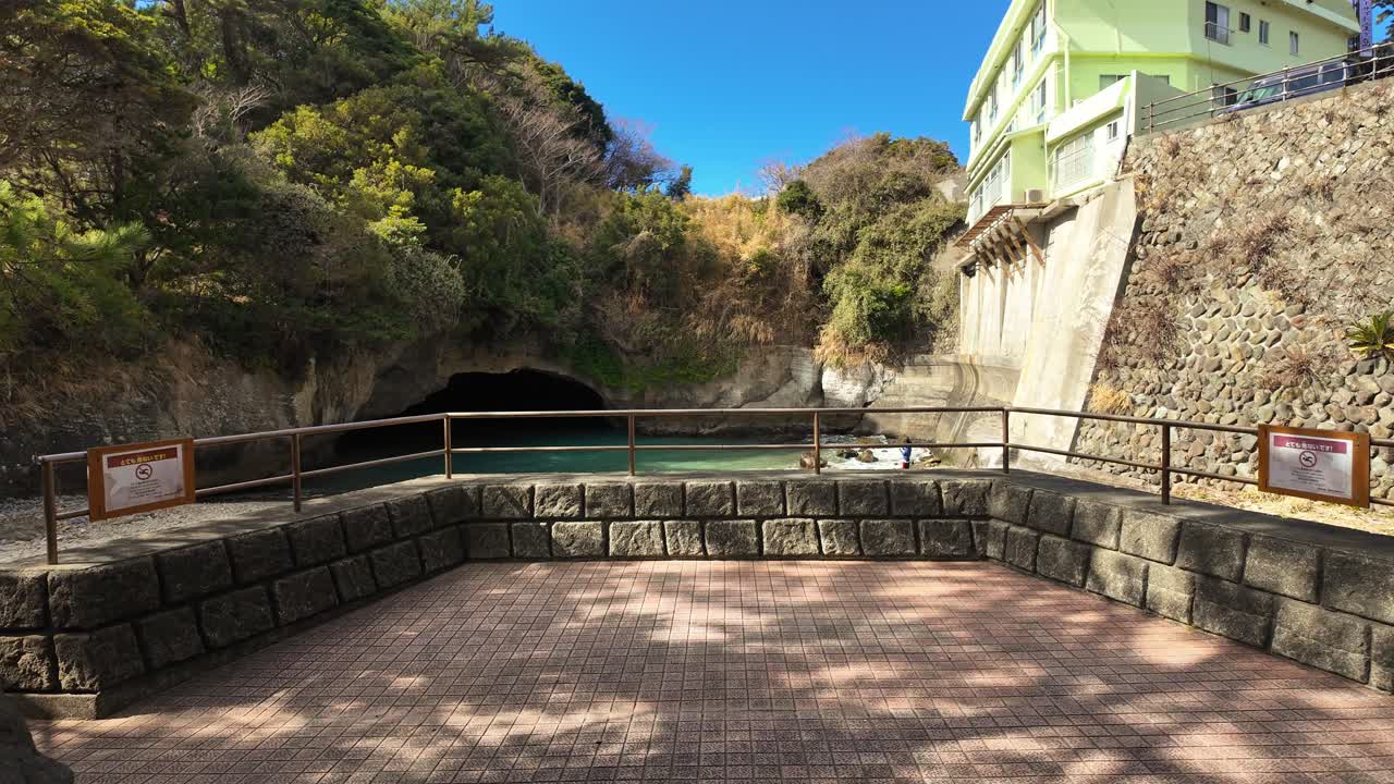 Perspective à la première personne marchant à travers un tunnel texturé en pierre pour révéler un point de vue ensoleillé surplombant la grotte marine de Ryugu et ses eaux turquoises au Japon