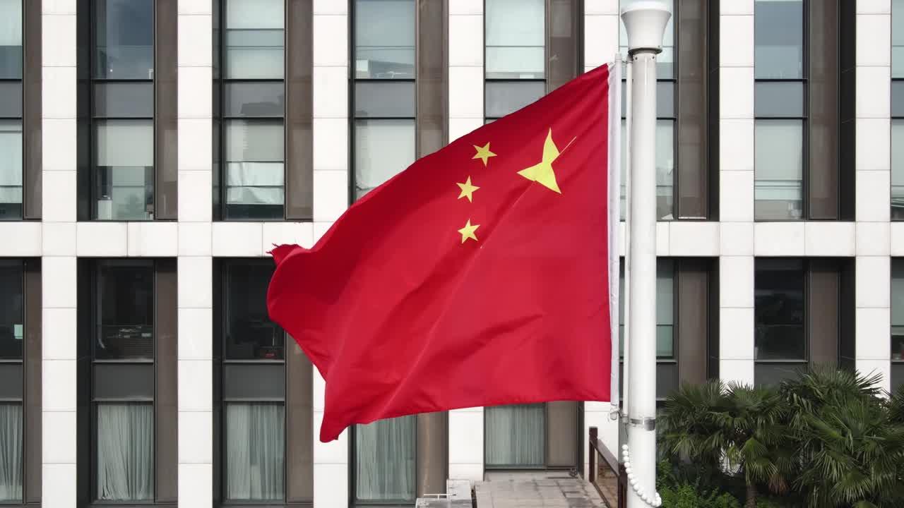 Bandeira Nacional Chinesa tremulando ao vento em frente a um edifício de escritórios moderno.