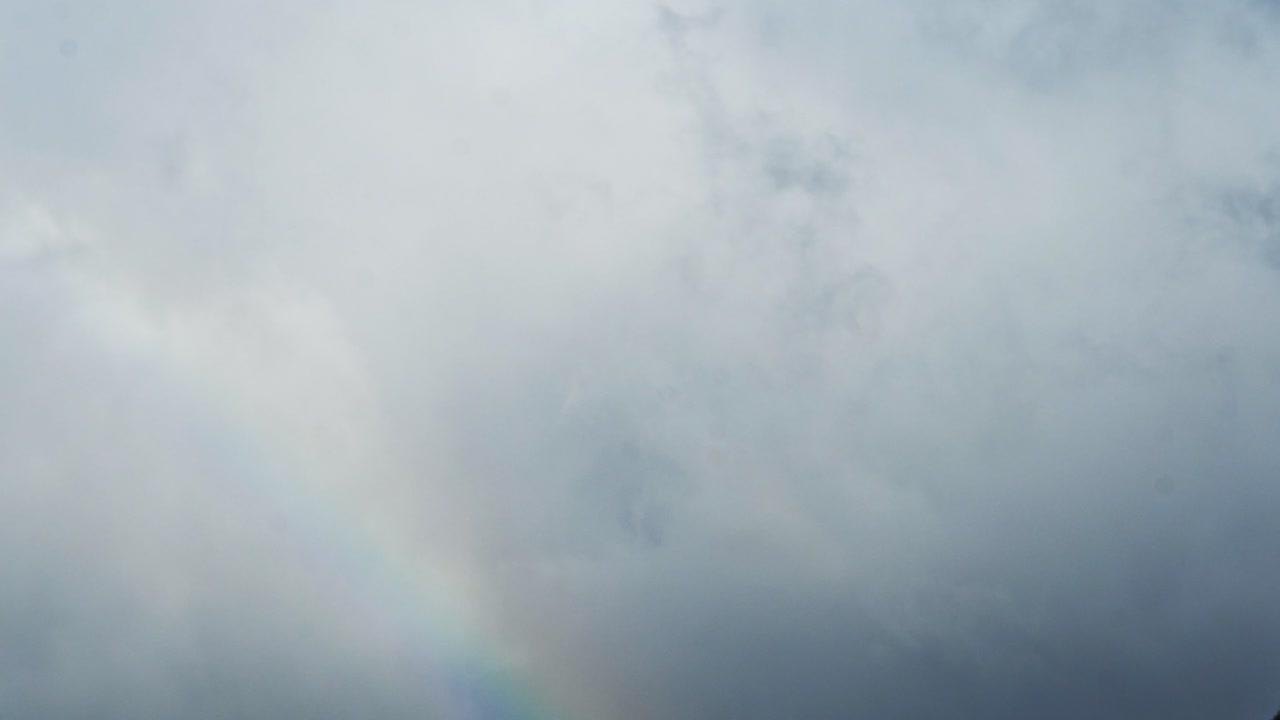 lapso de tiempo de un arco iris que aparece y se vuelve más vívido con nubes que se mueven detrás de él