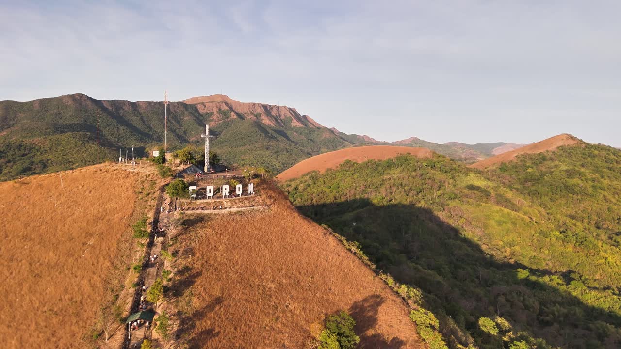 Elevated view from Mount Tapyas in Coron Town, Philippines, featuring the iconic CORON sign, summit cross, winding trail, and vast mountainous landscape during daylight