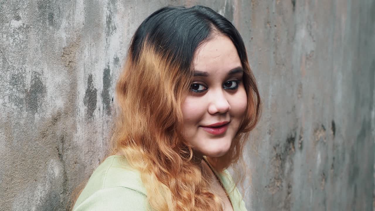 Smiling attractive young adult woman model looking at camera, happy beautiful 30s brunette lady professional pretty face dental smile posing stand alone indoors, slow motion close up view portrait.