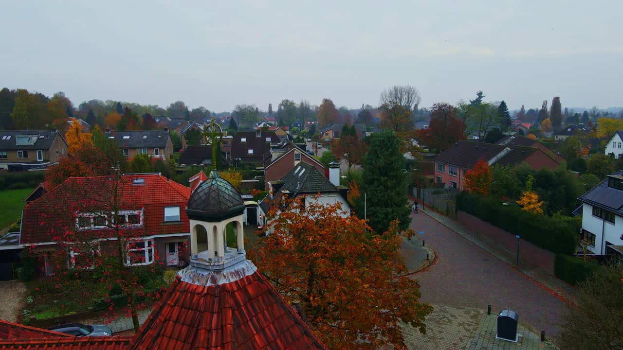 Dolly of an Old crucifix on top of church tower overlooking a peaceful suburban neighborhood on an overcast autumn day