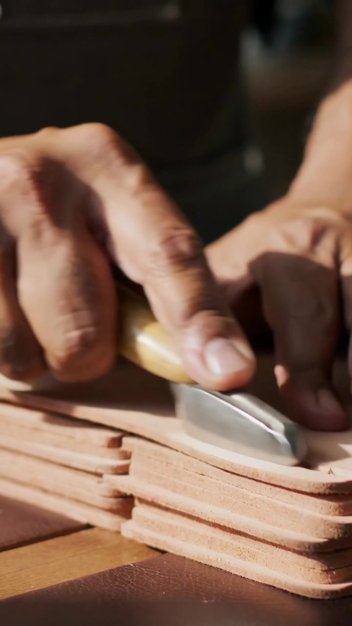 Vertical video: Placing burnisher, hands smoothing stacked leather edges on bench to finish, apron