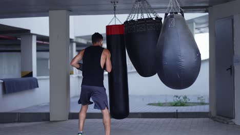 muscular male kickboxer training on different types of boxing bags