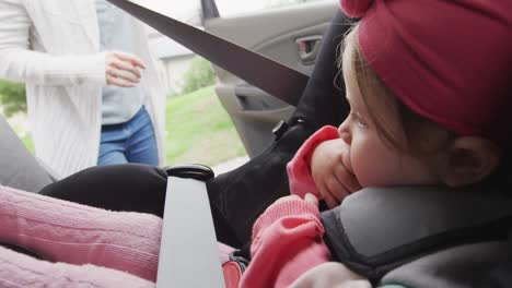 madre caucásica cerrando la puerta después de mantener a su bebé en el asiento de seguridad en el coche