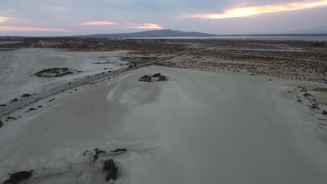 Aerial-drone-forward-moving-shot-over-dry-arid-landscape-road-with-vehicle-driving-towards-Mud-Volcano-in-background-at-Hingol-National-Park-in-Balochistan