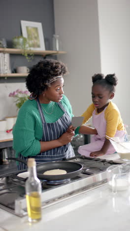 vertical video of african american mother and daughter frying pancakes in kitchen, slow motion
