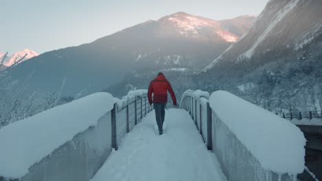 fixed shot, person in hiking clothes walking across snow covered bridge