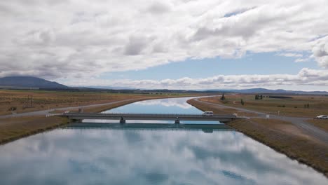 vuelo de drones sobre un canal azul que refleja el cielo mientras un camión cruza un puente