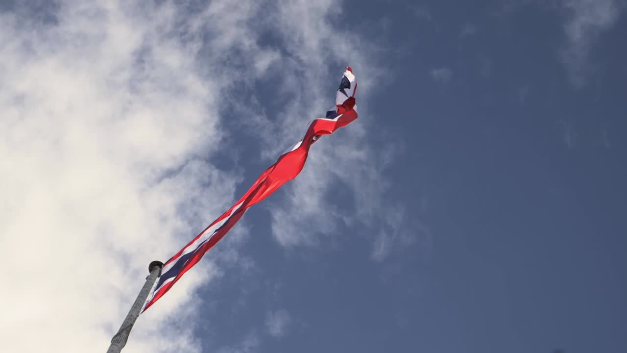 파란 하늘 과  ⁇  구름 을 배경 으로 한 기둥 에 태국 국기 를 흔들고 있다